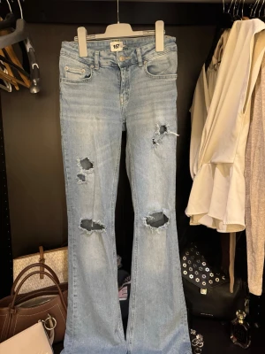 Bootcut jeans med slitningar från 157 - Ljusblå bootcut jeans från 157 med låg midja och slitna detaljer på benen. Jeansen har klassisk femficksdesign, dragkedja och knapp framtill. Tillverkade i jeansmaterial och har en avslappnad, trendig vibe.