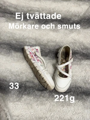 Vita ballerinaskor med blommönster - Säljer ett par vita ballerinaskor med fina blommiga detaljer i rosa och rött. Skorna har en rund tå och ett praktiskt band över foten för bättre passform. Perfekta för dig som gillar söta och färgglada skor med lite extra mönster.🌸Ej tvättade därav mörkare och smuts. Storlek 33 