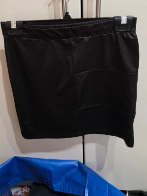 Svart kortkjol från att. Strl M - Svart kortkjol från att. i mjukt och stretchigt material med diskreta sömdetaljer framtill. Kjolen är tillverkad av 95% polyester och 5% elastan, vilket gör den bekväm och följsam. Perfekt för dig som gillar enkel och stilren design.