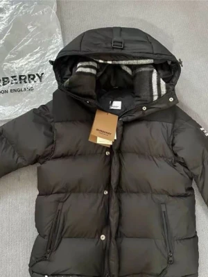 Svart pufferjacka - Svart pufferjacka med huva och coolt Burberry London England-märke på ärmen. Insidan har ett grått och vitt randigt foder som ger extra stilpoäng.