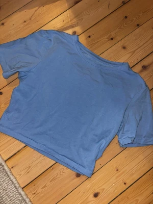 Ljusblå croppad t-shirt - Säljer en ljusblå croppad t-shirt med rund hals och korta ärmar. T-shirten är enkel och stilren utan mönster eller tryck, perfekt för dig som gillar en clean look. Materialet känns mjukt och lätt, troligtvis bomull. Ett lite hål vid ärmen, se sista bild
