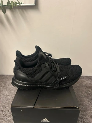 Adidas Ultraboost svarta sneakers - Svarta Adidas Ultraboost sneakers med stickad ovandel och platt sula. Skorna har snörning och en tydlig Boost-mellansula för extra komfort. Yttersulan är i gummi med Continental-mönster för bra grepp. Perfekta för dig som gillar stilrena och sportiga skor.