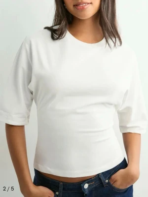 Nelly knyt topp - Säljer en vit croppad topp med korta ärmar och rund halsringning. Toppen har öppen rygg med breda band som knyts i en rosett bak. Tillverkad i mjuk bomull, perfekt för en trendig och avslappnad look. Nästan aldrig använd, pris kan diskuteras!🫶🏻