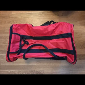 Stor röd resväska med svarta detaljer - Säljer en stor och rymlig röd resväska med svarta handtag och axelrem. Väskan har flera dragkedjefack och är tillverkad i slitstark polyester. Perfekt för dig som behöver mycket plats när du ska iväg på resa.