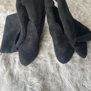 Svarta höga stövlar med klack - Svarta höga stövlar i mockaimitation med spetsig tå och smal hög klack. Dragkedja på insidan och mjukt material som ger en snygg passform. Perfekta för att lyfta din outfit med en edgy vibe.