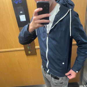 Mörkblå vindjacka med huva - Säljer en tvär fet mörkblå windbreaker perfekt inför hösten. Storlek S. Trendig och passar till allt. Vid fler frågor och funderingar är det bara att höra av dig 