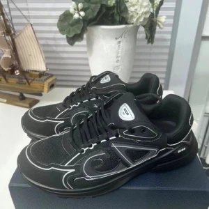 Svarta b30 - Säljer ett par svarta Dior sneakers med vita kontrastdetaljer och logga på sidan och plösen. Skorna har rund tå, platt sula och snörning. Materialet är en mix av mesh och syntet, vilket ger en sportig och modern vibe. Perfekta för dig som gillar exklusiva streetwear.