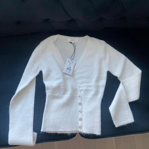 Alpackaull Stickad top XS - Högst bud 474kr!  Väldigt populär och många är intresserade. Säljs snabbt, så skynda att köpa. Först till kvarn! Stickad omlottkofta i alpackamix med v-ringning. Koftan är vit och har knappar i sidan. Den har normal passform, figurnära midja, lång ärm och bred ribbstickning i nederkant.  Intressekoll. Helt ny. 