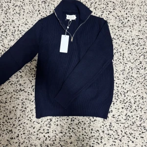 Marinblå stickad half zip från Maison Margiela - Riktigt snygg marinblå stickad tröja från Maison Margiela med half zip och hög krage. Tröjan är ribbstickad och har långa ärmar, perfekt för lager på lager. Klassisk och stilren design som funkar till allt. Men den e lite stor för M storlek, L och XL storlek funkar också.
