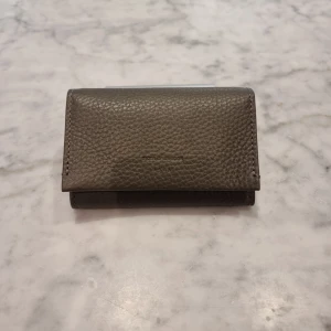 Grå plånbok från Tiger of Sweden - Snygg grå plånbok från Tiger of Sweden i äkta skinn. Plånboken har ett stilrent och kompakt format, praktisk knappstängning och flera fack för kort. Perfekt för dig som gillar minimalistisk design och kvalitet.