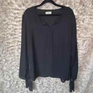 Transparent blus med strass och knyt - Blusen är väldigt fin och har snygga knytband vid ärmsluten. Den är halvtransparent. Fin strassdetalj vid kragen. Blusen är skir och luftig. Ser lyxig ut.