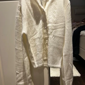 Vit kofta från Meet Me There S/M - Superfin vit kofta från Meet Me There med snyggt stickat mönster framtill och knappar. Koftan är långärmad och stilren. Perfekt att slänga över en topp. Den är även helt ny och oanvänd med prislapp kvar