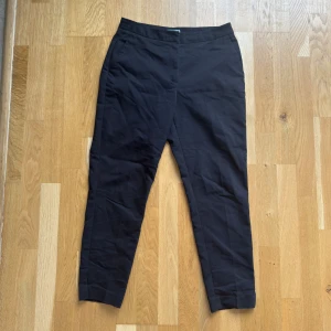 Svarta kostymbyxor från H&M, strl 36 - Svarta kostymbyxor från H&M i storlek 36. Byxorna har en klassisk rak passform med croppad längd och är tillverkade i en mjuk blandning av bomull och polyester. Perfekta för en clean och stilren look.