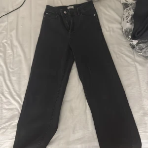 Svarta raka jeans från Lindex - Svarta jeans från Lindex i rak modell med hög midja. Klassisk femficksdesign och dragkedja med knapp framtill. Jeansen är tillverkade i ett stadigt denimtyg som ger en snygg siluett och passar till många olika stilar.