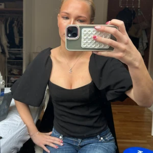 Svart Bikbok topp med puffärmar - Säljer en svart topp med markerad sweetheart-urringning och stora puffärmar. Toppen är figurnära och har en stilren, modern look som passar perfekt till jeans eller kjol. Materialet känns slätt och något stadigt, vilket ger en snygg siluett.