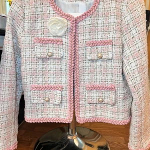 Set tweed jacka och ljusrosa kjol + present( midja kedja i bild) - Supersöt kortkjol i ljusrosa och vitt rutigt tyg med inslag av guldtråd. Kjolen har en guldkedja med dekorativa rosor och en vit blomma framtill. Materialet är tweed-liknande och kjolen är fodrad med vitt tyg för extra komfort. Perfekt för dig som gillar chic och trendig stil.