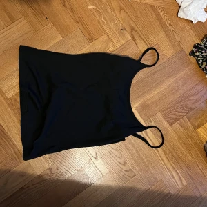 Svart enkel linnetopp - Säljer en svart, stilren linnetopp med smala axelband. Toppen har en rak passform och är tillverkad i ett mjukt material som känns skönt mot huden. Perfekt att matcha med jeans eller kjol för en clean look.