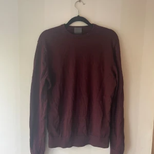 Vinröd merinoullströja från H&M - Vinröd långärmad tröja från H&M i mjuk merinoull. Klassisk rund hals och ribbade muddar vid ärmslut och nederkant. Perfekt för dig som gillar enkel och stilren design med en mörk ton. Snygg att matcha med jeans eller chinos.