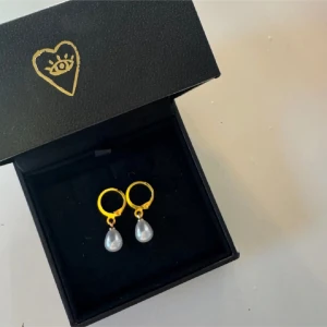Guldörhängen med droppformade pärlor - Snygga örhängen med guldfärgade ringar och droppformade vita pärlor som hänger ned. Perfekt för dig som gillar klassisk stil med en modern twist.