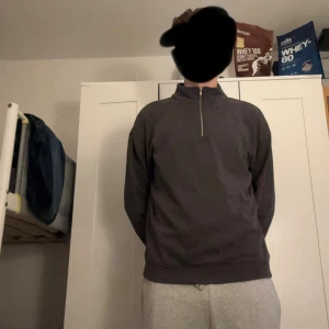 Mörkgrå tröja med half zip - Mörkgrå långärmad tröja med hög krage och half zip-dragkedja framtill. Enkel och stilren design, perfekt för lager-på-lager. Tröjan har normal passform och är tillverkad i ett mjukt material som känns skönt mot huden.