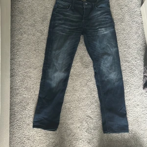 Mörkblå jeans från Jack & Jones 30/30 - Säljer ett par mörkblå jeans från Jack & Jones i modellen Comfort/Mike. Jeansen har snygga slitningar. Byxorna är bara använda några fåtal gånger och har inga tecken på användning. Storlek 30/30