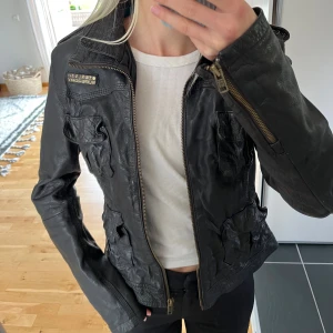 Svart skinnjacka från Superdry - Säljer en svart skinnjacka från Superdry med coola fickdetaljer och dragkedja framtill. Jackan har lång ärm, flera fickor med lock och en snygg krage. Insidan är fodrad med turkos tyg för extra kontrast. 