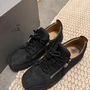 Svarta sneakers från Giuseppe Zanotti - Säljer ett par svarta sneakers från Giuseppe Zanotti med snygga silverfärgade dragkedjor på sidorna och snörning framtill. I stolek 44 men rekommenderas för 43, Skorna har en diskret glittrig yta och är tillverkade i mocka med läderdetaljer på insidan. Perfekta för dig som gillar stilrena men ändå unika skor. Skorna är nästan oanvända så i väldigt bra skick men lådan är i lite sämre men funkar absolut ändå!! Nypris-5000-6000kr mitt pris 2199