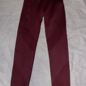 Vinröda seamless leggings XS 157 - Snygga vinröda seamless leggings från 157 i storlek XS. De har ribbade detaljer och är tillverkade i ett stretchigt syntetmaterial som sitter tight och bekvämt. Perfekta för träning eller chill dagar. Färgen är djup vinröd och modellen är högmidjad.