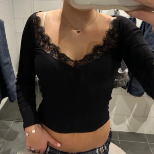 Svart ribbad topp med spets från Zara - Säljer en supersöt långärmad topp från Zara med ribbad struktur och v-ringad halsringning med spetsdetaljer. Storlek S❤️
