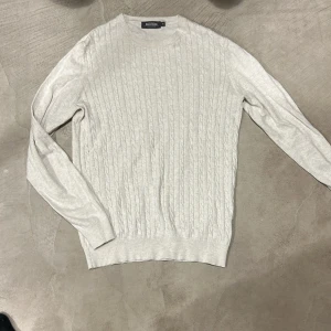 Ljusbeige kabelstickad tröja Dressmann - Säljer en ljusbeige kabelstickad tröja från Dressmann i storlek M. Tröjan är tillverkad i mjuk bomull och har rund halsringning samt långa ärmar. Perfekt för lager-på-lager och enkel att matcha med jeans eller chinos.