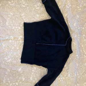 Mörkblå stickad tröja med kontrastsömmar - Mörkblå stickad tröja från Zara med ribbad midja och ärmslut. Tröjan har tunna ljusblå kontrastsömmar längs ärmar och mitt fram samt bak, vilket ger en clean och modern vibe. Rund halsringning och långärmad modell, perfekt för lager på lager under kyliga dagar. Tröjan är i storleken S