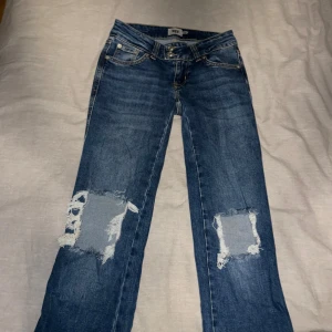 Blå slitna jeans från 157, XS - Blå jeans från 157 i storlek XS med full längd. Modellen har låg midja och raka ben, samt slitna detaljer och stora hål vid knäna för en cool, avslappnad look. Klassisk femficksdesign och tillverkade i jeansmaterial.Använda en gång!