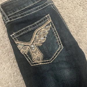 Mörka jeans med broderade bakfickor - Mörkblå botcut jeans från Gina, med design på bakfickorna. 