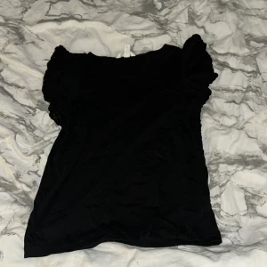 Svart blus med puffärm från H&M - Svart blus från H&M i storlek XS med korta puffärmar och lätt volangdetalj vid axlarna. Mjuk och skön bomullskvalitet som sitter snyggt. Perfekt för dig som gillar en enkel men ändå söt look.