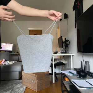 Grått linne - Säljer ett enkelt och stilrent grått linne med smala axelband och rak passform. Linnet är kort och har en minimalistisk look som passar dig som gillar clean stil. Perfekt för varma dagar.