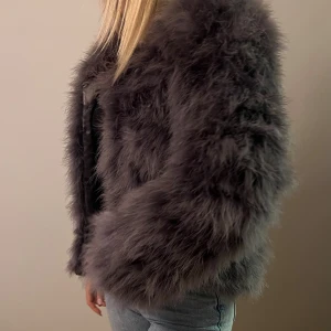 Mörkgrå fluffig pälsjacka - Supermjuk och fluffig pälsjacka i mörkgrå ton. Jackan har lång ärm, rak passform och är helfodrad. Perfekt för dig som vill sticka ut och hålla dig varm med stil. Ingen synlig knäppning framtill för en clean look.