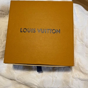 Louis Vuitton svart rutig bälte - Snyggt svart bälte från Louis Vuitton med klassiskt rutigt mönster och stor LV-logga i metall som spänne. Bältet kommer i original ask, dustbag och med blått Louis Vuitton-band. Perfekt accessoar för att lyfta din outfit. 110cm 