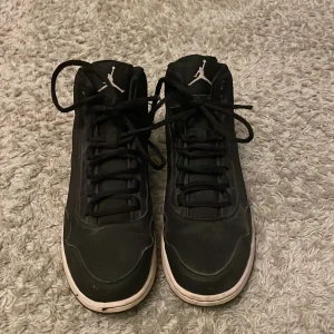 Svarta Nike Air Jordans sneakers - Svarta Nike Air Jordans sneakers med vita detaljer och klassisk Jumpman-logga på sidan och plösen. Skorna har snörning, rund tå och vit platt sula. Tillverkade i syntetmaterial och skinn för en sportig och clean look.