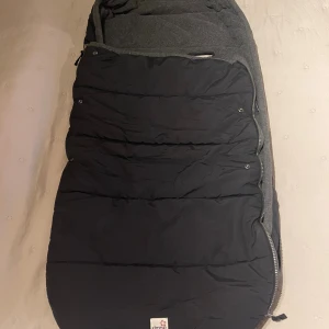 Åkpåse från Simple world - Svart åkpåse med grått fleecefoder. Kan öppnas från båda håll, och om man vill kan hela ovandelen plockas bort.