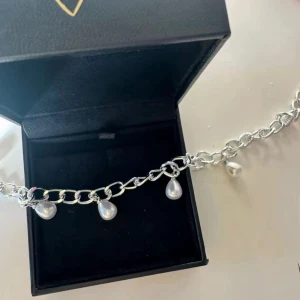 Pärlhalsband Silver - Kedjehalsband i silverfärg med fem droppformade pärlor som hänger längs kedjan. Ger en cool och trendig vibe, perfekt att styla med både basic och mer edgy outfits. Pärlorna är vita och ger ett snyggt kontrast mot den grova kedjan.