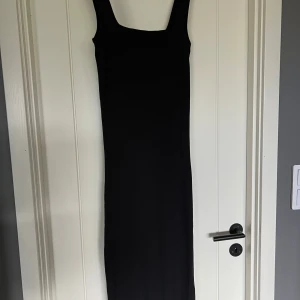 Svart ribbad långklänning - Svart långklänning med ribbad struktur och breda axelband. Klänningen har en rak och tight passform som framhäver siluetten. Aldrig använd.  
