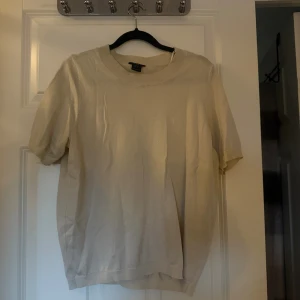 Beige stickad kortärmad tröja H&M - En stilren beige stickad tröja från H&M med korta ärmar och rund halsringning. Perfekt för lager-på-lager eller som den är. Enkel och clean design som passar till det mesta. Materialet är mjukt och bekvämt.