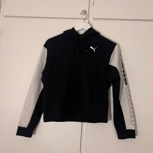 Svartvit tunn hoodie från Puma - En tunnare hoodie från Puma. Lätt croppad, med luva. På vänster arm står det ”PUMA” i svart och vitt. 