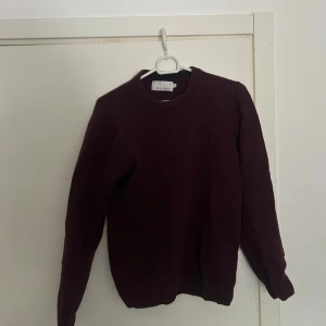 Vinröd stickad tröja från Casual Friday - Mysig vinröd stickad tröja från Casual Friday med rund halsringning och långa ärmar. Perfekt för kyliga dagar och enkel att matcha med jeans. Klassisk modell med ribbade muddar vid ärmslut och nederkant.