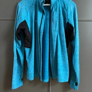 Blå tröja/kofta från Dobsom Sweden - Snygg blå tröja från Dobsom Sweden i storlek M. Tröjan har svarta detaljer på ärmarna, dragkedja framtill och långärmad design. Perfekt för dig som gillar sportig stil och vill ha en tröja som funkar till träning och utomhusaktiviteter.