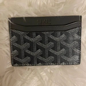 Svart Goy4rd plånbok med mönster - Snygg och stilren plånbok från Goy4rd i svart med ikoniskt grafiskt mönster i vitt. Slimmad design med flera fack för kort, tillverkad i exklusivt skinn. Perfekt för dig som vill ha något lyxigt och unikt i fickan. Levereras med originalask och tag.