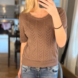 Brun stickad tröja från VILA - Säljer en brun stickad tröja från VILA i storlek XS. Tröjan har korta ärmar, rund halsringning och ett snyggt hålmönster i hela plagget. Perfekt för lager-på-lager och funkar året runt. Supermjuk och skön att bära.