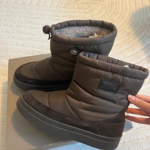 Bruna vinterboots från Gant - Säljer ett par bruna vinterboots från Gant med vadderad ovandel och mjukt foder. Skorna har grov sula för extra grepp, dragsko upptill och detaljer i mocka. Perfekta för kalla dagar när du vill hålla fötterna varma och torra. Storlek 40 men passar mig Bra som är 39