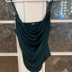 Mörkgrön linnetopp från Bik Bok - Snygg mörkgrön linnetopp från Bik Bok med draperad front och tunna axelband. Toppen har en elegant, loose passform och är tillverkad i mjukt syntetmaterial som faller fint. Perfekt för dig som gillar stilrena och trendiga plagg.