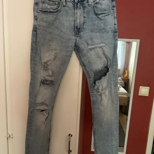 Ljusblå ripped jeans från Denim & Denim strl: 32/30 - Säljer ett par ljusblå jeans med slitna detaljer och stora hål på båda benen. Modellen är slim fit med klassisk femficksdesign och knappstängning. Jeansen har en modern, streetig look och är tillverkade i bomull med lite stretch för skön passform.